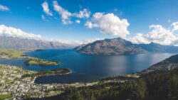 buildings near body of water and mountains under clear blue sky and white clouds at daytime